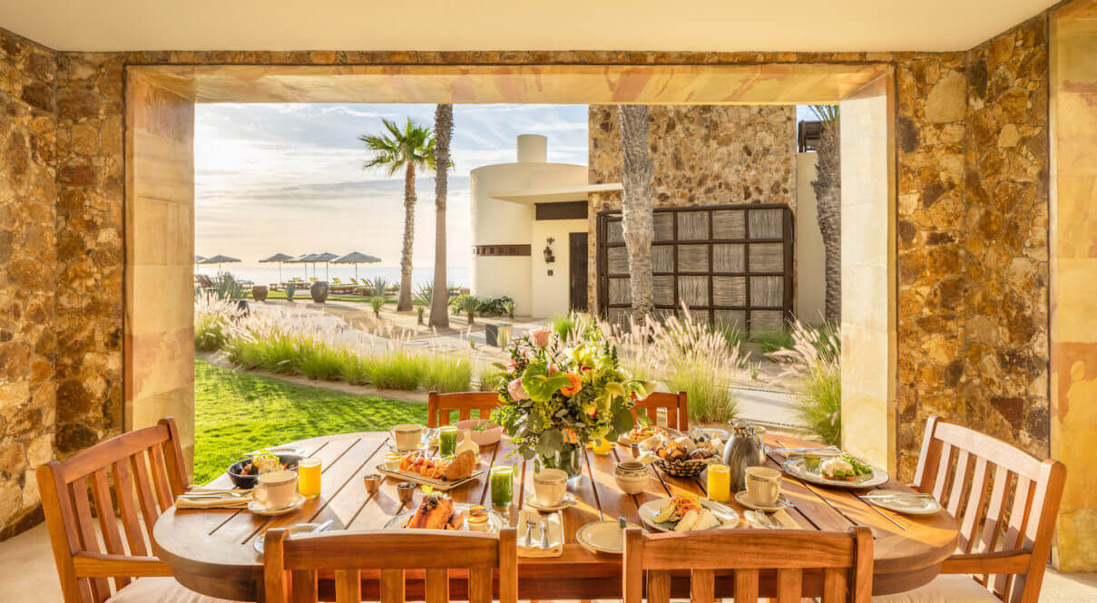 Interior of the Two-Bedroom Casita at Waldorf Astoria Los Cabos Pedregal, featuring a table, chairs, large windows, and stunning beach views.