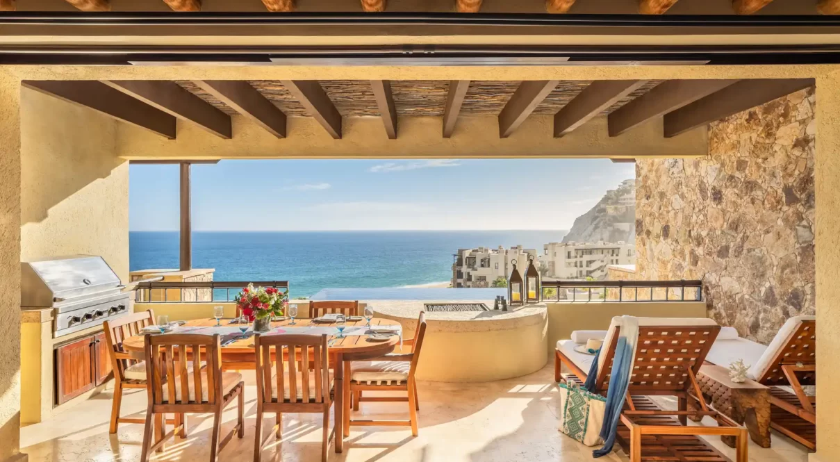 Covered patio with dining table, grill, and lounge chairs overlooking the sea at WA Los Cabos Pedregal.