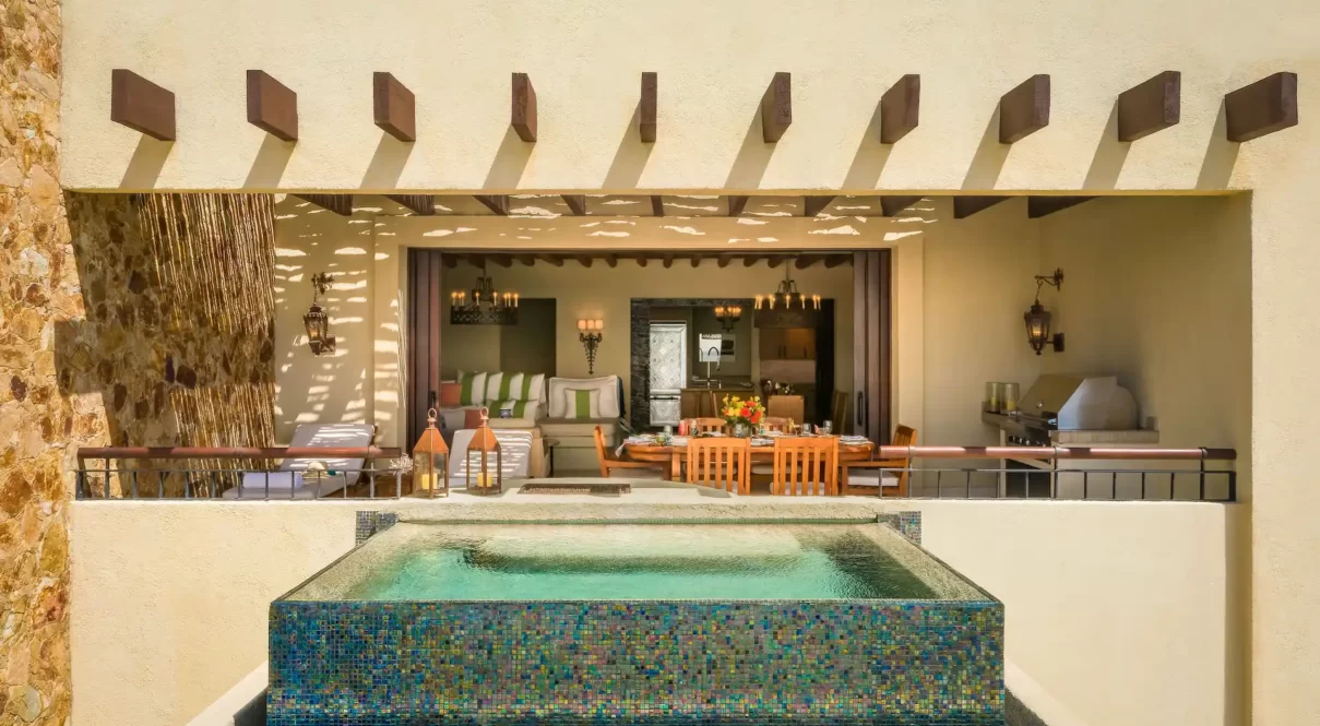 Covered patio with mosaic hot tub, lounge chairs, and grill in a luxury cliffside villa.