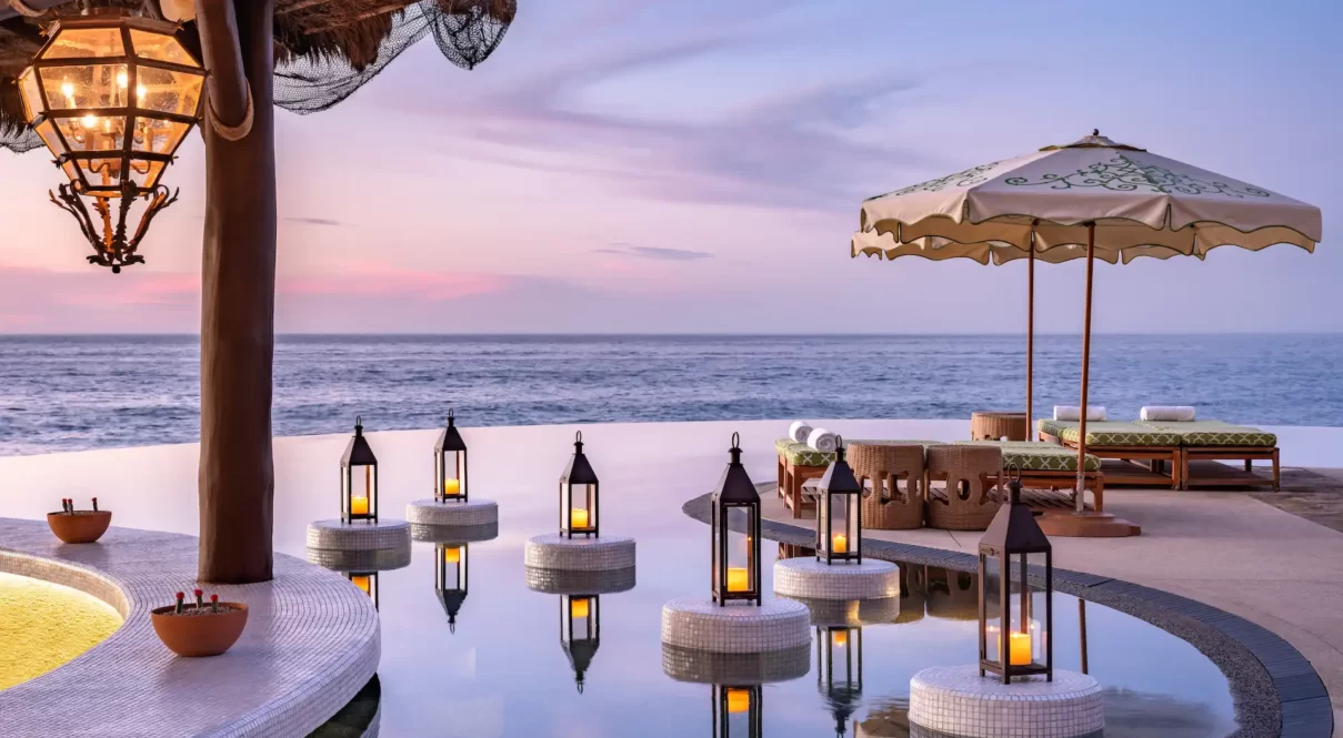 Infinity pool with lanterns and lounge beds at sunset in a tropical seaside resort.