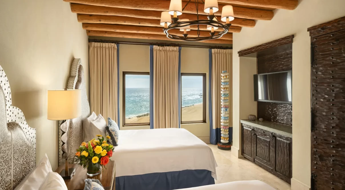Ocean-view room with two queen beds, wood beams, chandelier, and coastal decor.