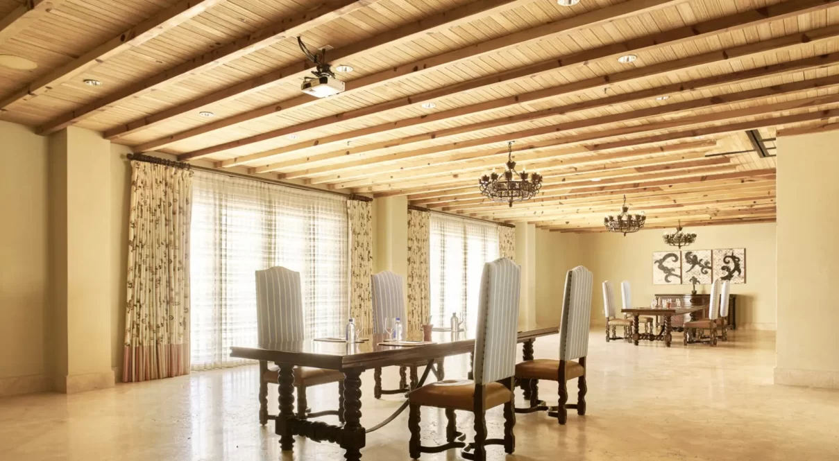 Rustic chic room with wood beams, chandeliers, and long tables set for dining or meetings.