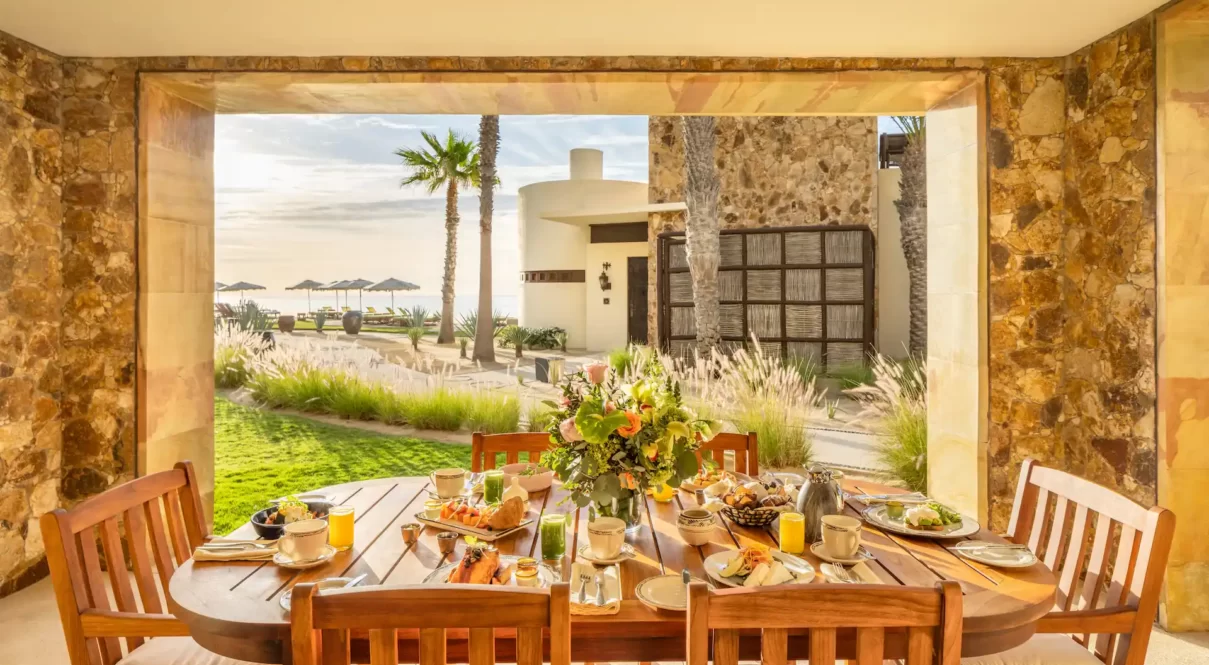 Covered patio with breakfast table, floral centerpiece, and ocean view in a tropical resort setting.