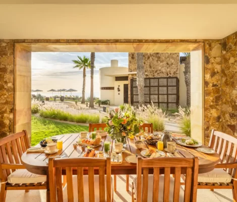 Covered patio with breakfast table, floral centerpiece, and ocean view in a tropical resort setting.