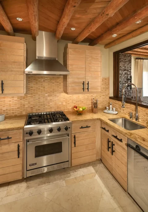 Rustic kitchen with wood beams, stone counters, and open view to dining area with chandelier.