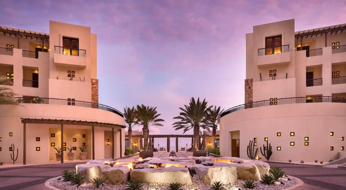 Symmetrical resort buildings with fire pit and desert landscaping at sunset.