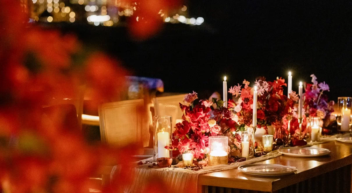Evening table with red florals, candlelight, and elegant tableware in a scenic outdoor setting.