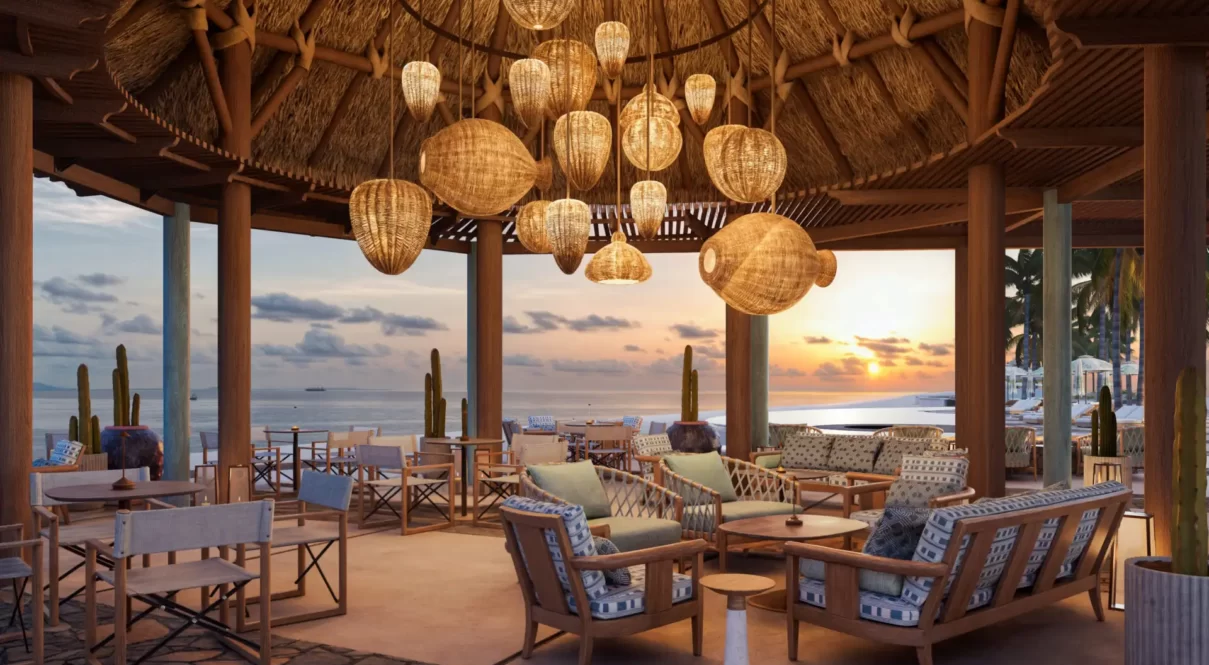 Beachside lounge with thatched roof, woven lights, and ocean sunset view in a tropical retreat.